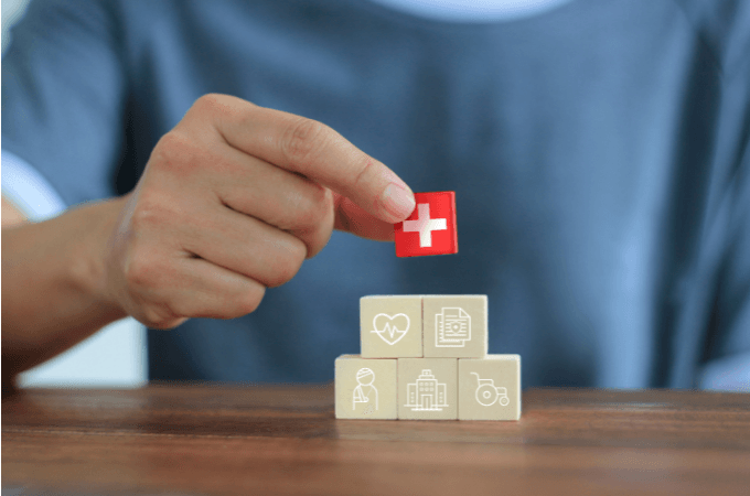 Cumberland Life Insurance - Picture of a Life Insurance client holding a red cross symbol. He is wearing a blue T-shirt and placing the the block on a pyramid of 5 other blocks that have symbols representing the pillars of happiness and family wellbeing.