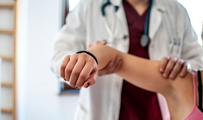 Medico che esamina il braccio di un paziente, in un ambiente chiuso. Il medico indossa un camice bianco e uno stetoscopio. Il braccio del paziente è sollevato.