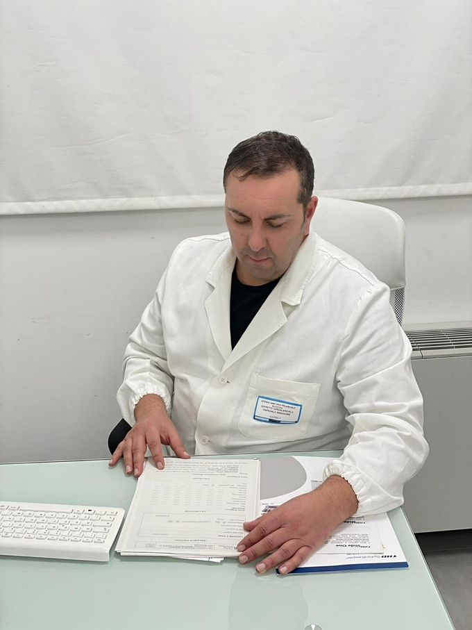 Un medico in camice bianco esamina dei documenti seduto alla scrivania di un ufficio.