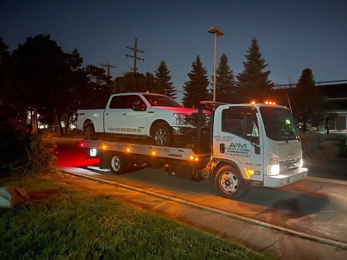 A white truck is being towed by a tow truck at night.