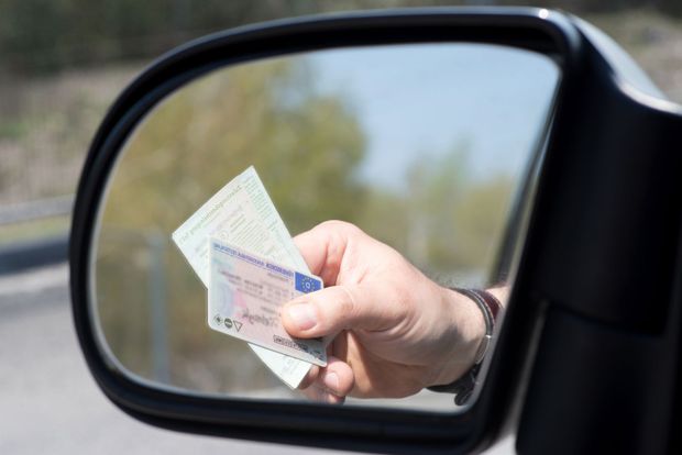 A hand holding identification cards is reflected in a car side-view mirror.