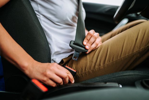 A person in a white t-shirt and tan pants buckling their car seat belt.