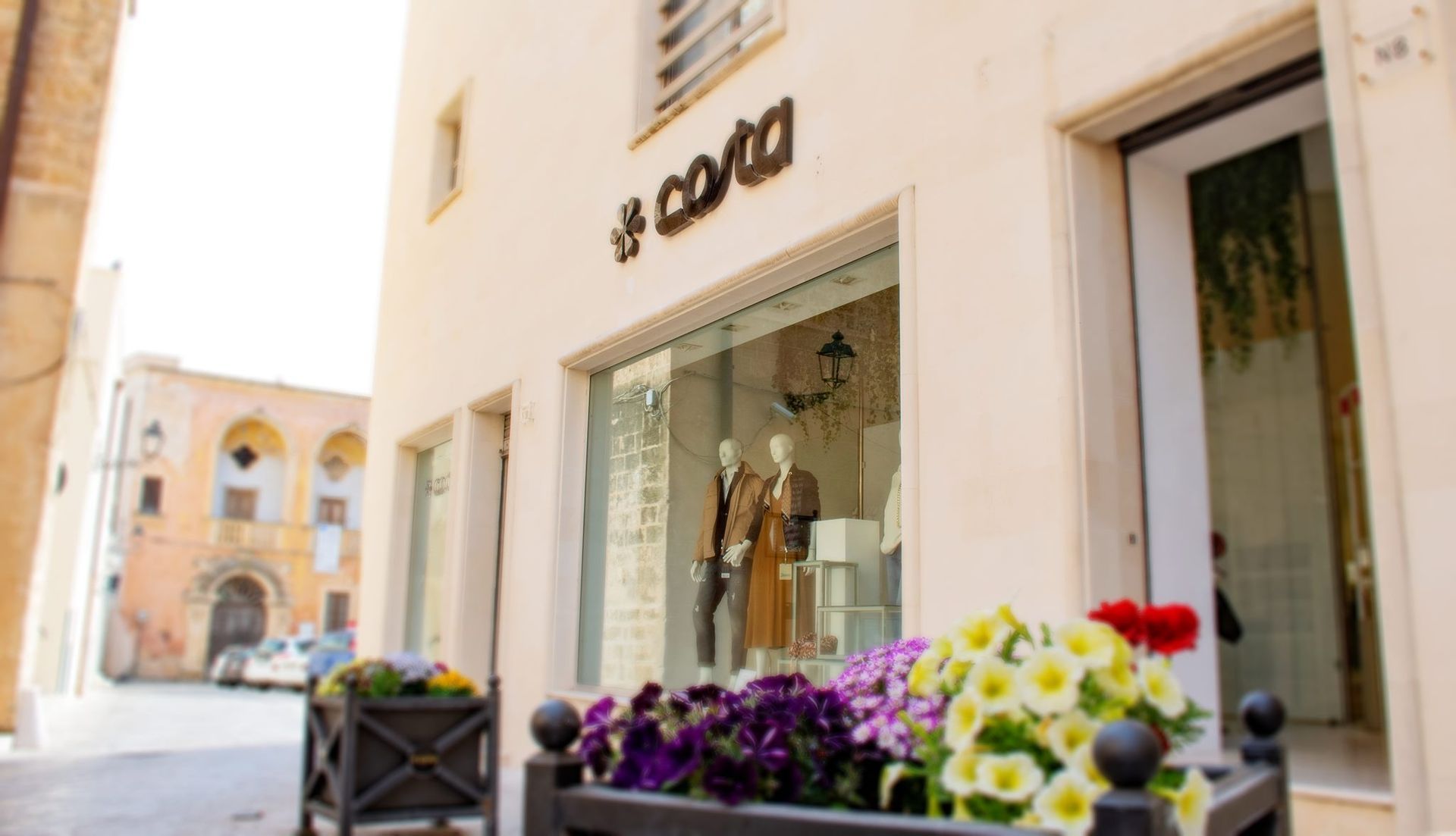 Esterno di un negozio di abbigliamento con manichini in vetrina. Fiori in una fioriera di fronte.