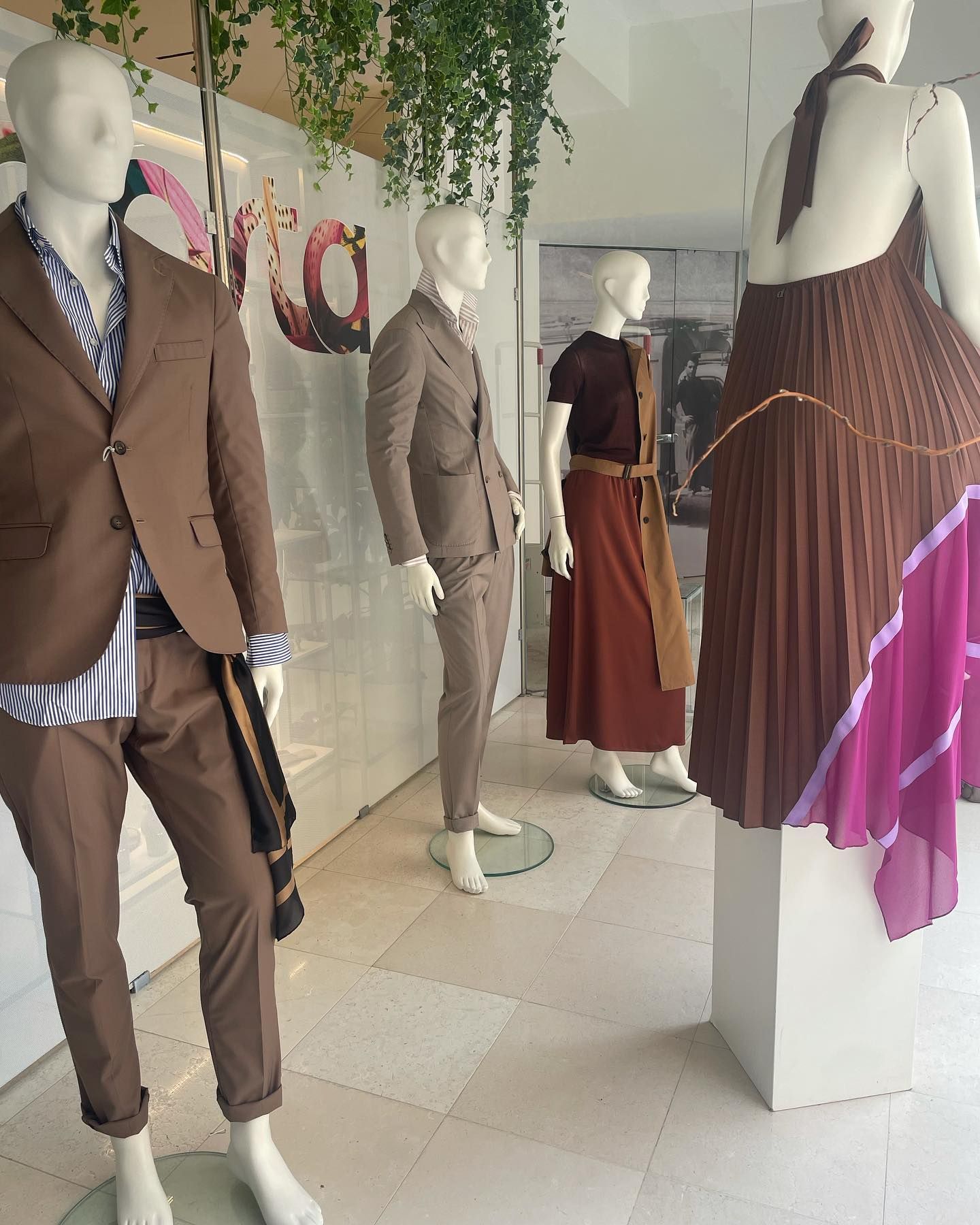Vetrina con manichini in vari abiti marroni, tra cui un tailleur e degli abiti.