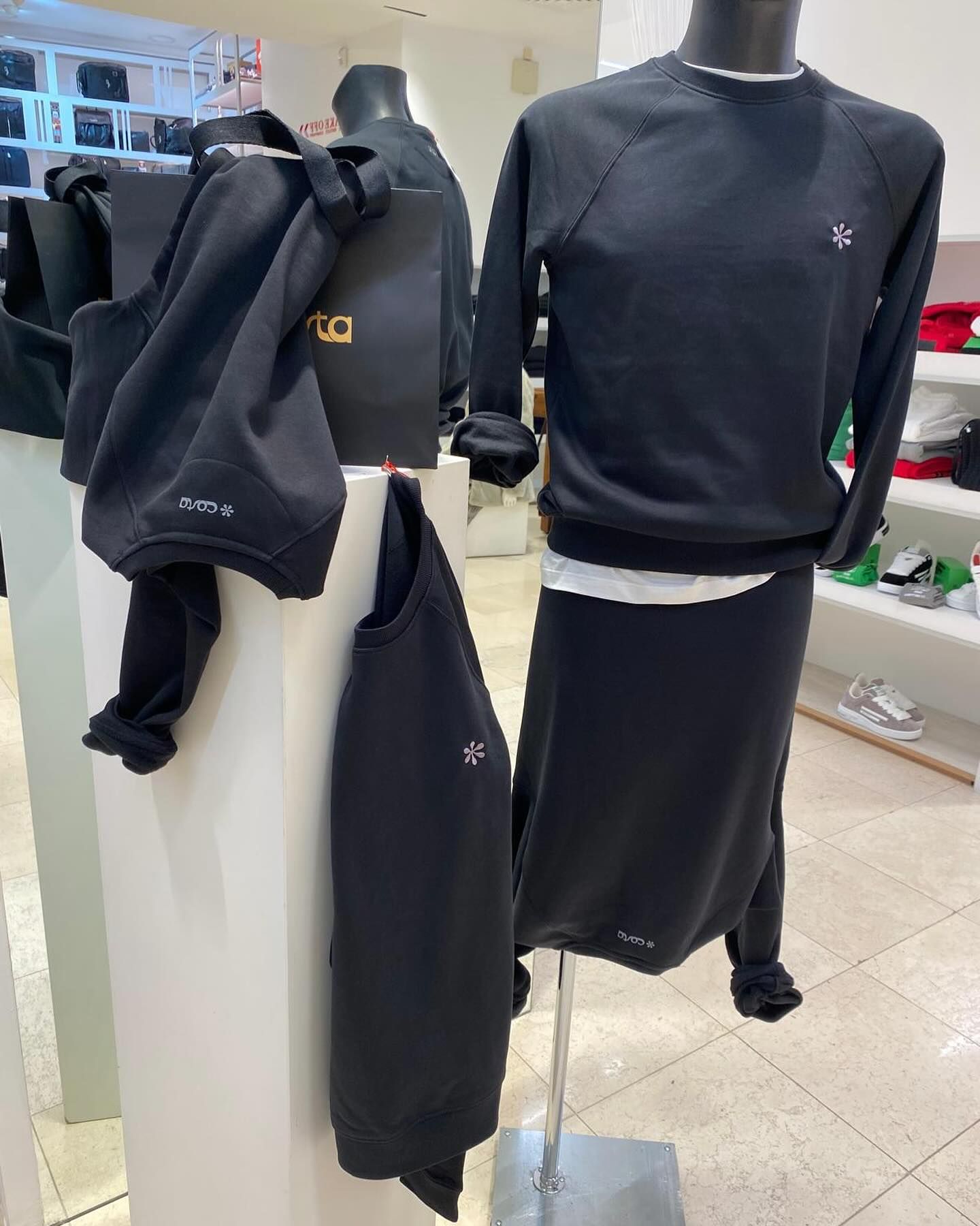 Espositore di abbigliamento nero in un negozio. Un completo felpa e gonna su un manichino. Altre felpe su un'asta e una borsa tote.