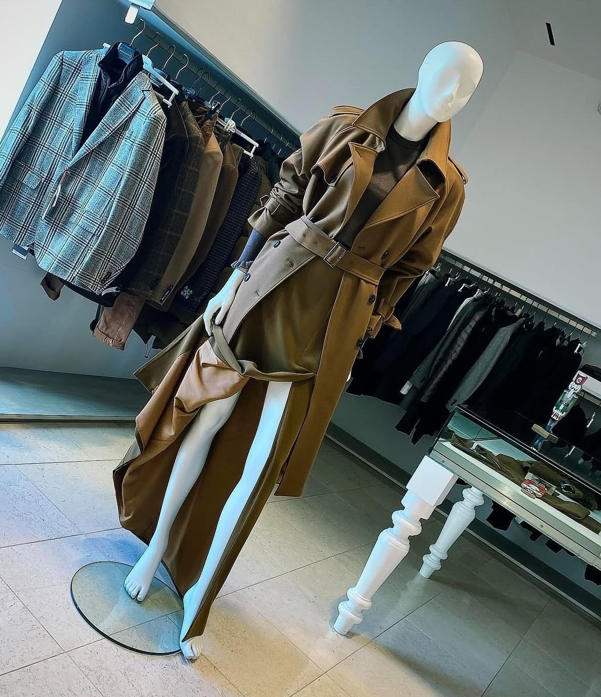 Manichino con trench marrone; appendiabiti sullo sfondo.