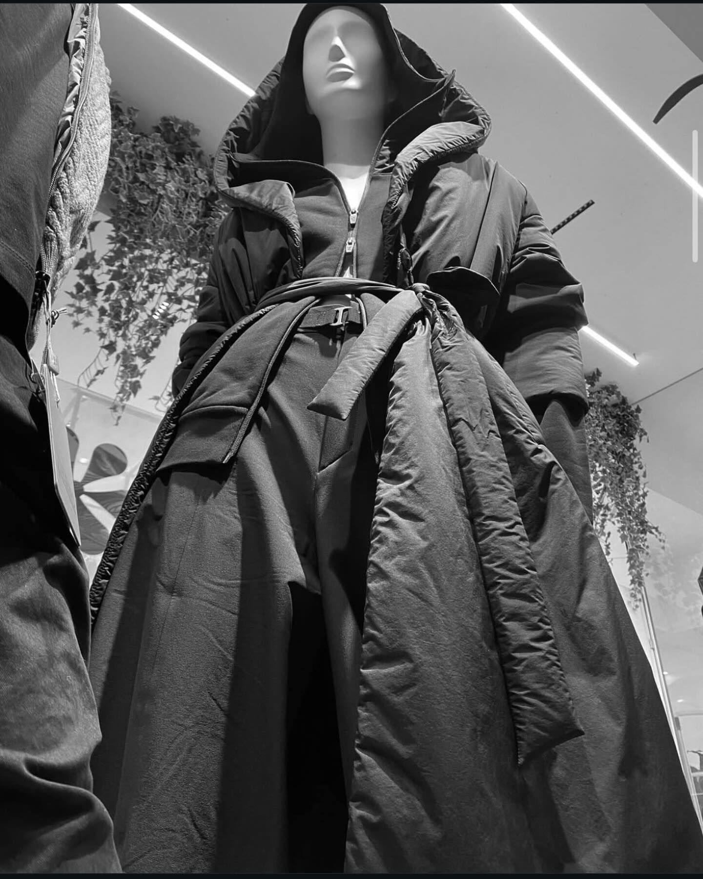 Manichino con un lungo cappotto nero con cappuccio e cintura in vita.