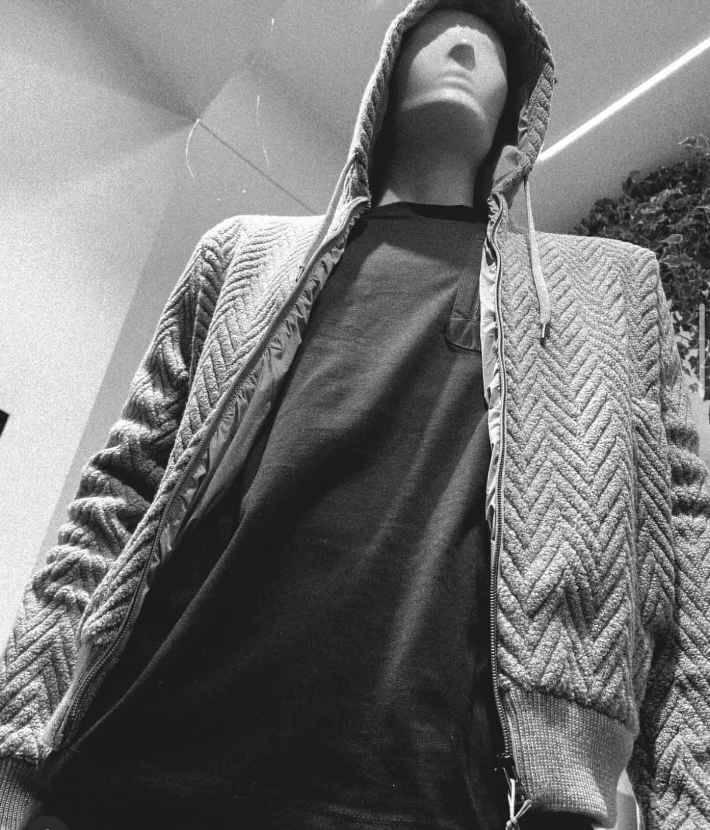 Manichino che indossa una felpa grigia con cappuccio e cerniera a fantasia sopra una maglietta scura.