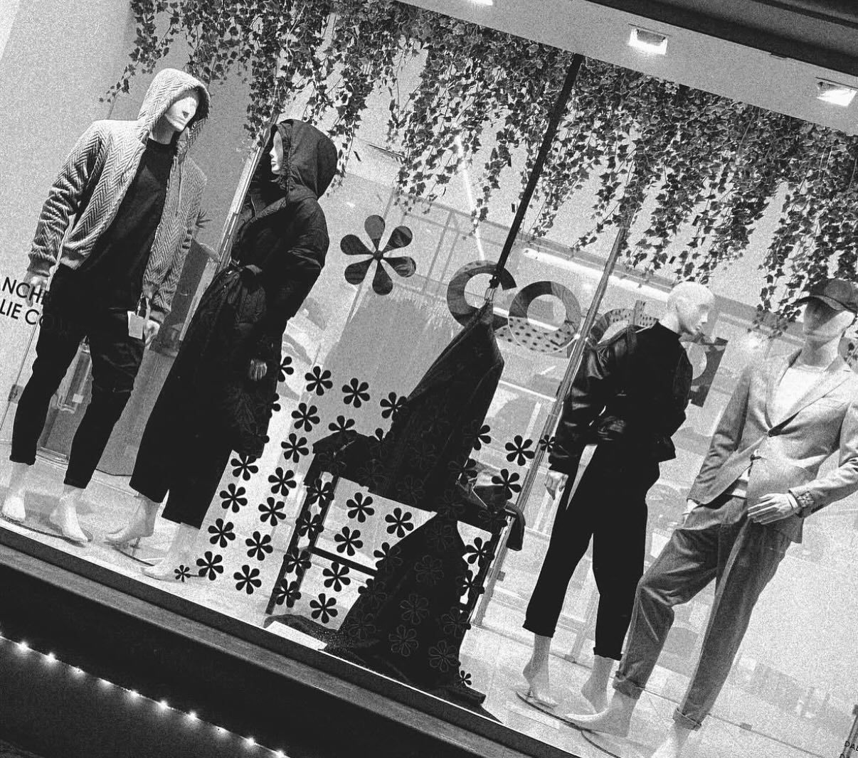 Vetrina con manichini che mostrano vari stili di abbigliamento, in scala di grigi.