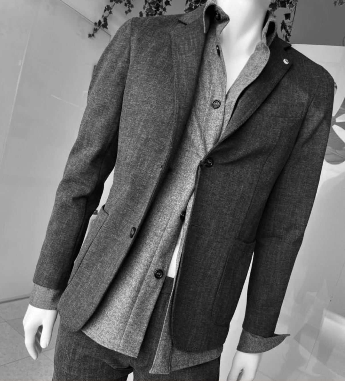 Un uomo con occhiali da sole, camicia e maglione al collo è in piedi contro un muro di pietra.