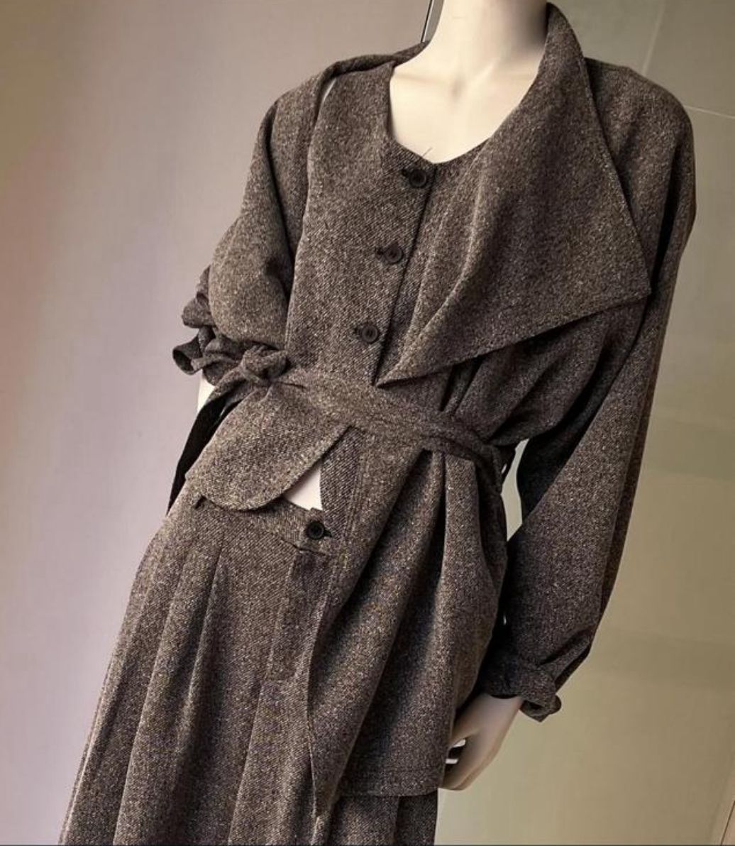 Donna in abito marrone e cappotto in un negozio, che cammina. Manichini sullo sfondo.