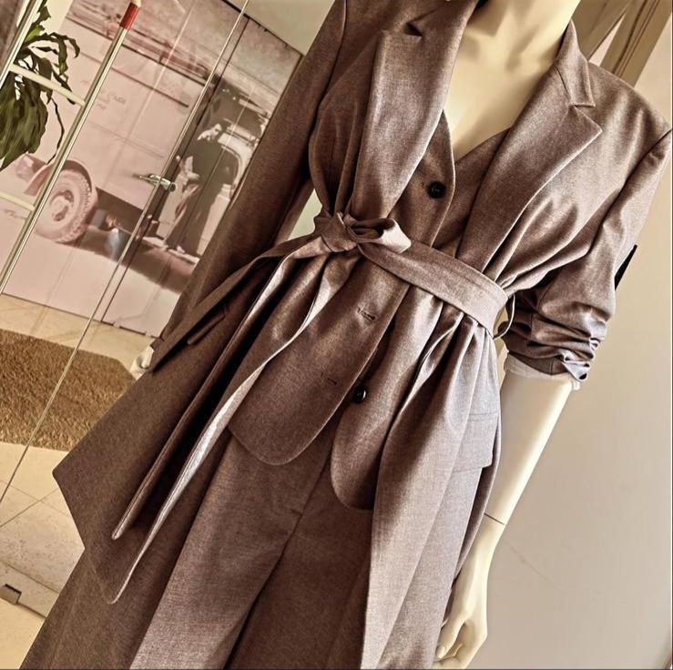 Un uomo e una donna seduti su una piccola sedia davanti a un negozio di abbigliamento. L'uomo con occhiali da sole, cappotto e pantaloni. La donna in giacca e cravatta.