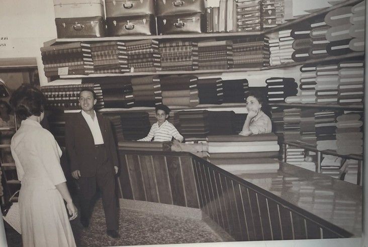 Due manichini in una vetrina, uno con un cappotto marrone, l'altro con un piumino, davanti a un edificio sullo sfondo.