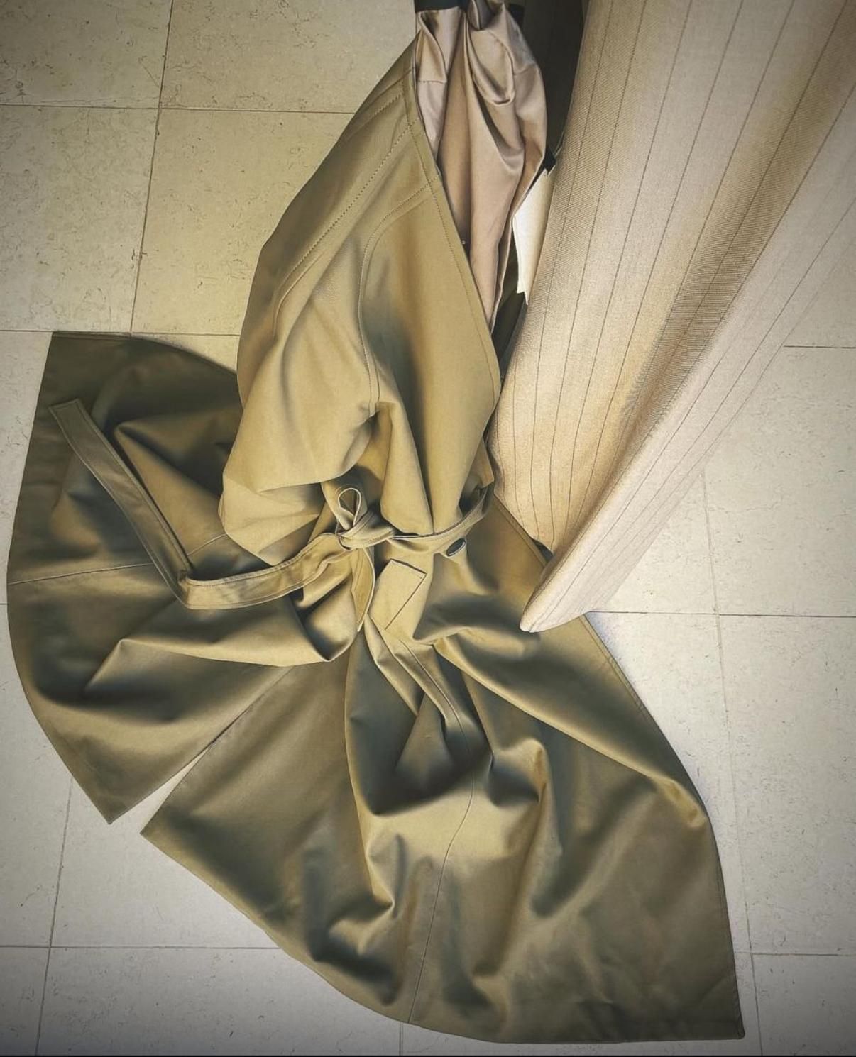 Donna in abito marrone e cappotto in un negozio, che cammina verso la telecamera. Manichini dietro di lei.