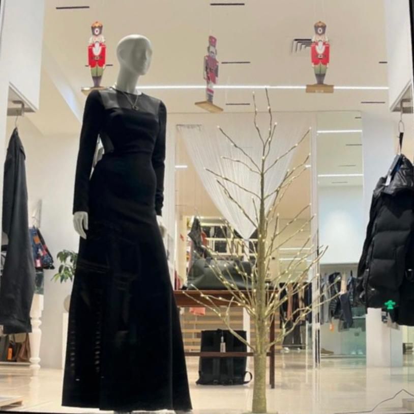 Vetrina con manichini che indossano vari abiti scuri. Decorazioni floreali e rampicanti in bianco e nero.