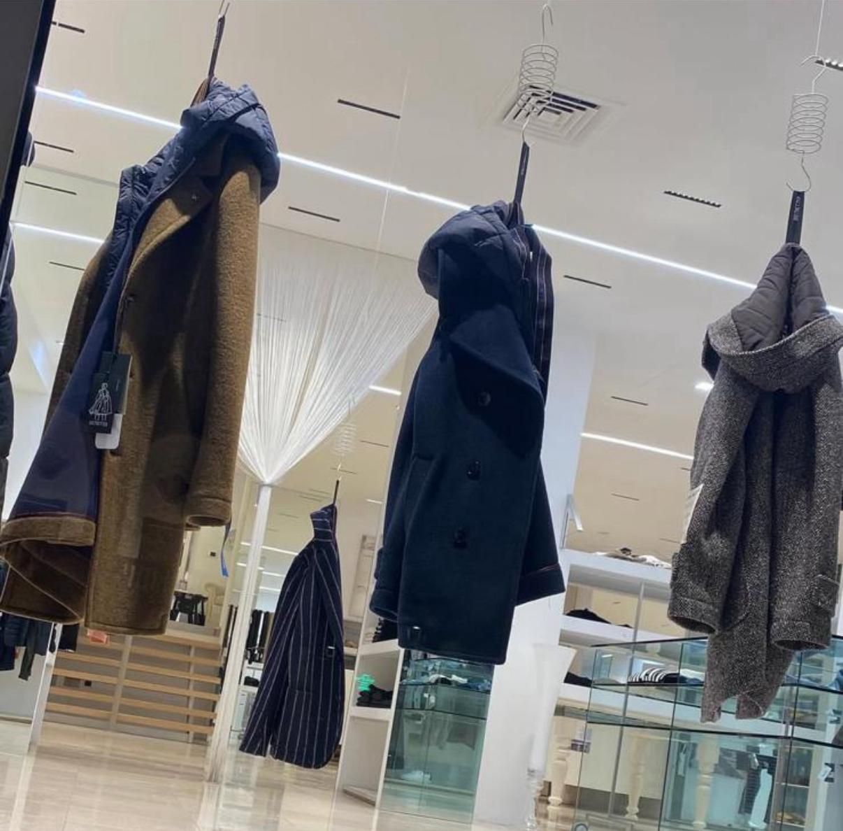 Manichino che indossa un trench marrone in un negozio di abbigliamento, con scaffali di vestiti sullo sfondo.