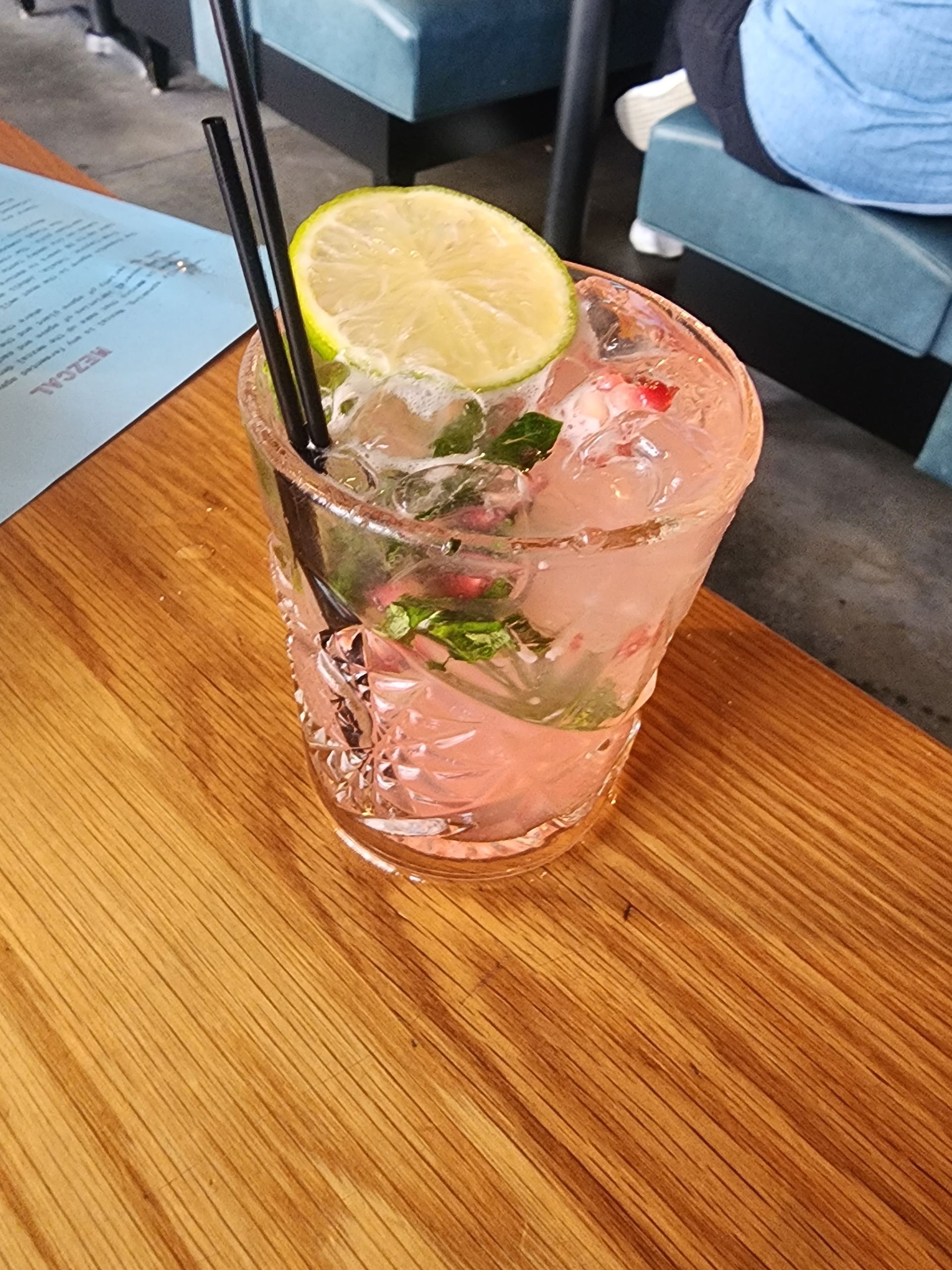 Pink cocktail with lime and mint in a decorative glass, on a wooden table.