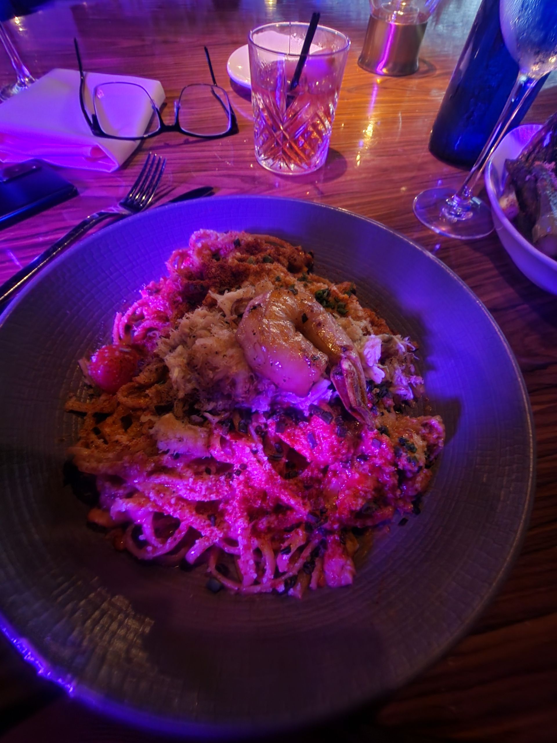 Pasta dish with shrimp and sauce on a table with drinks and glasses.