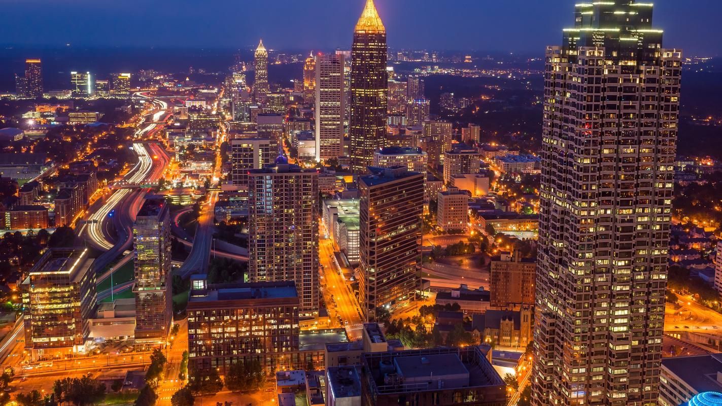 Atlanta skyline at dusk with lit skyscrapers, roads, and city lights.