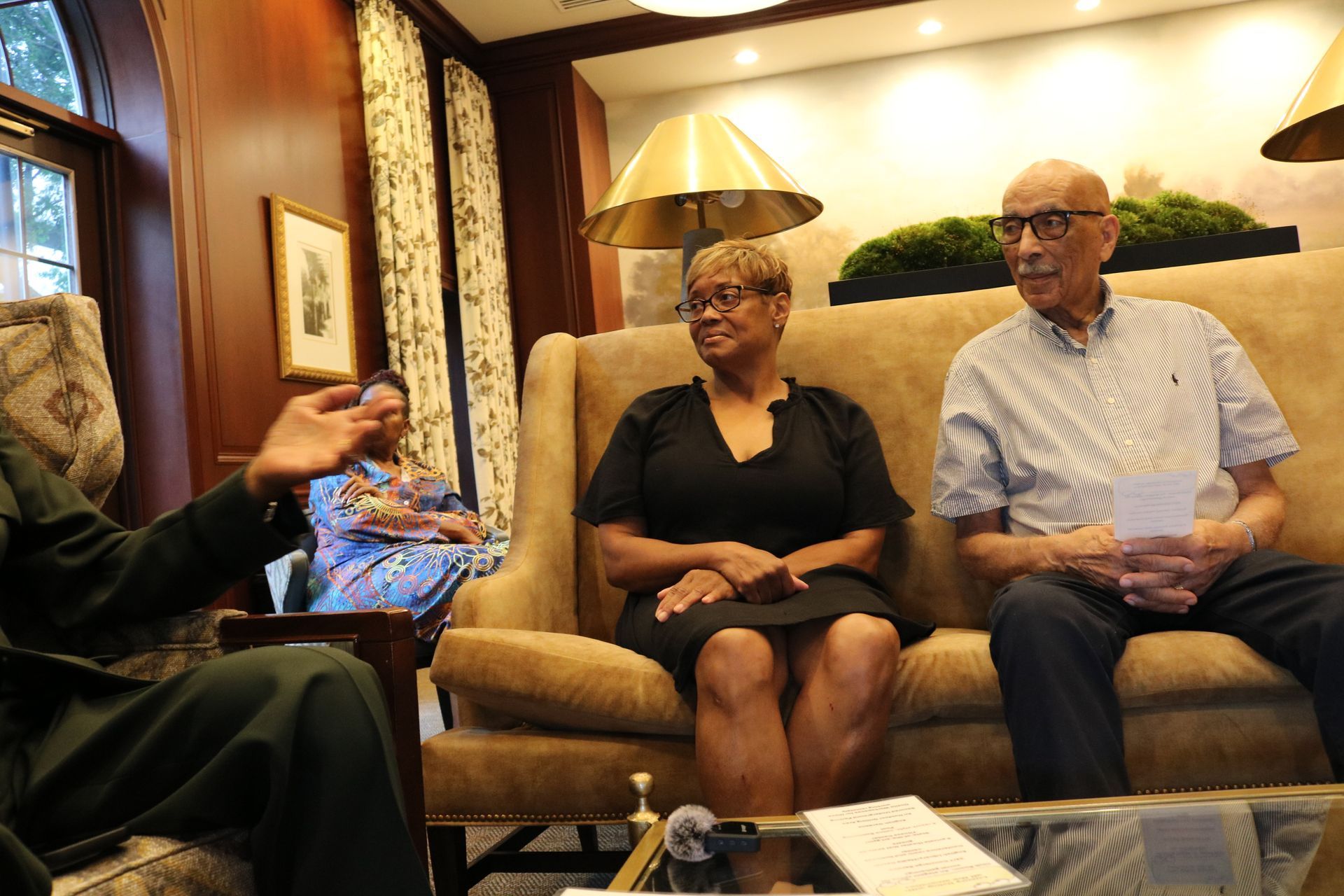 People seated on a sofa indoors, one person speaking, two listening.