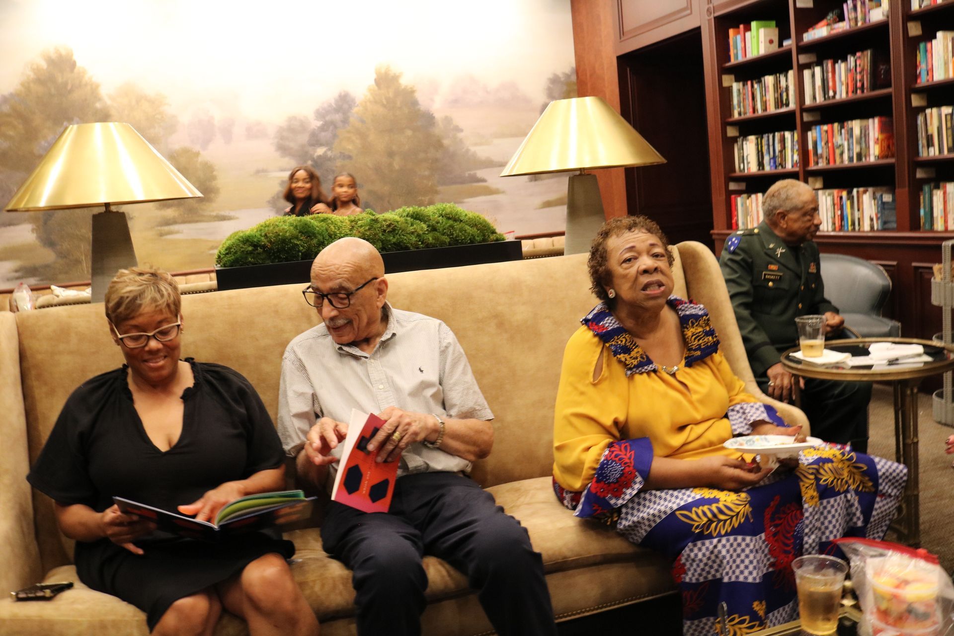 People seated on a couch in a library. One person holds a book, others look around.