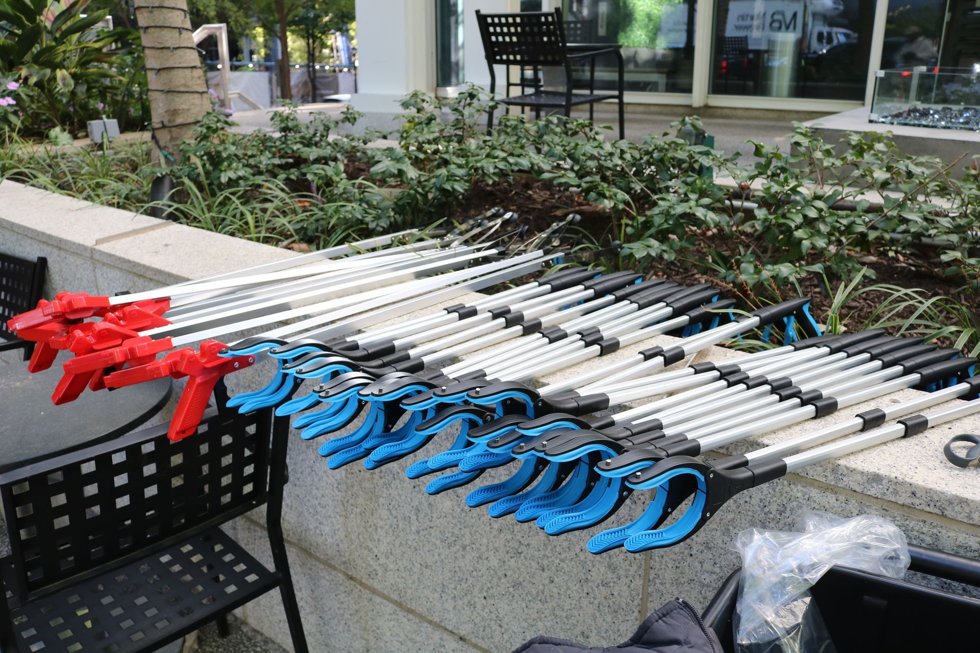 Rows of grabber tools, red and blue handles, lined up on a low wall outdoors.