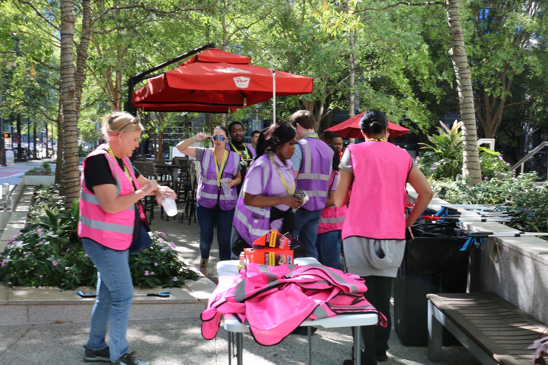 People wearing pink vests and purple shirts gather outdoors near a red umbrella.