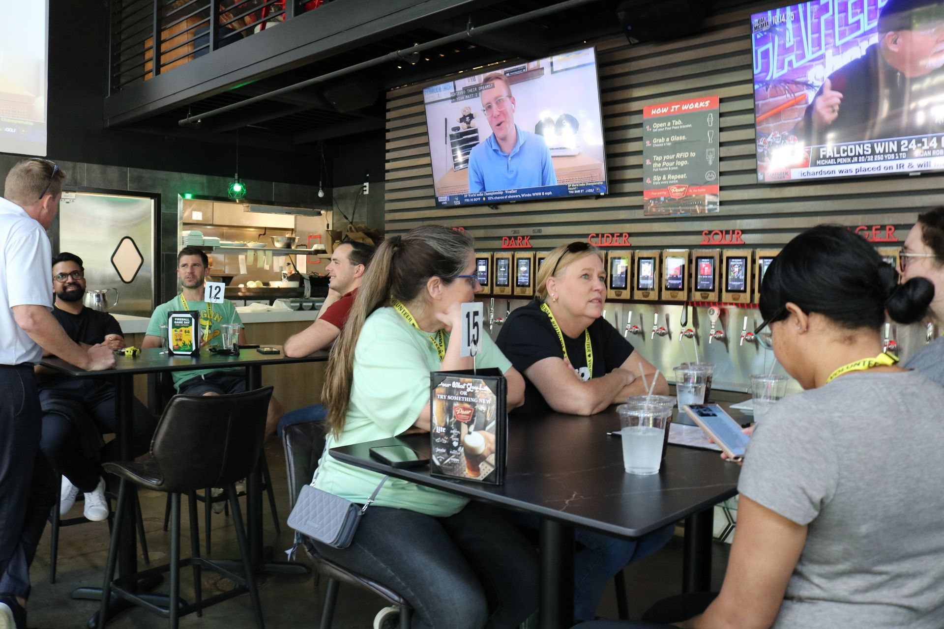 People sitting at tables in a bar, watching TV and talking.