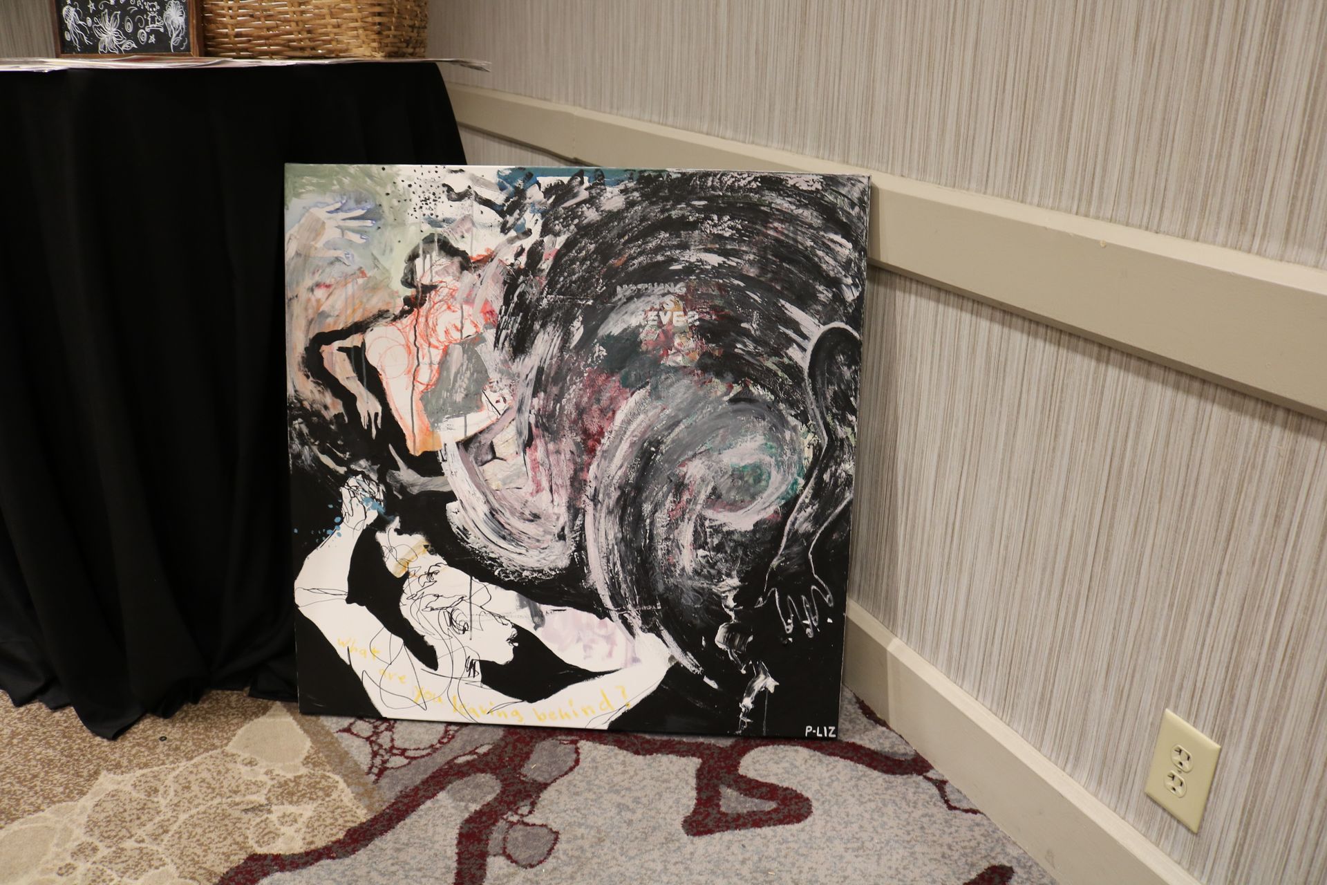 Abstract painting leaning against a wall, mostly black with white and colored brushstrokes.