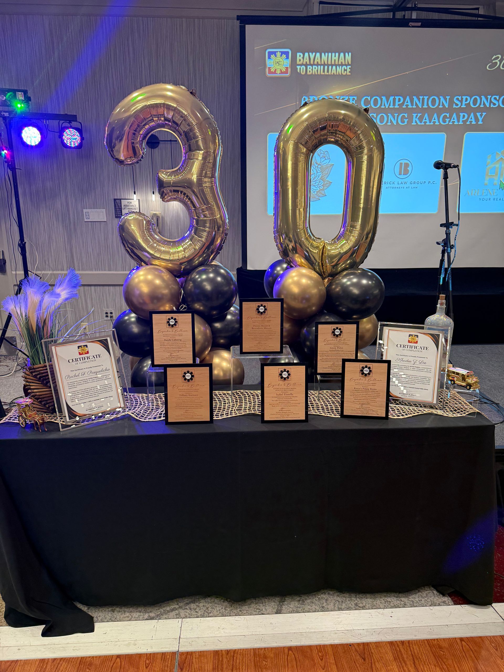 A table display celebrating a 30th anniversary. Gold balloons, plaques, and black and gold decor.