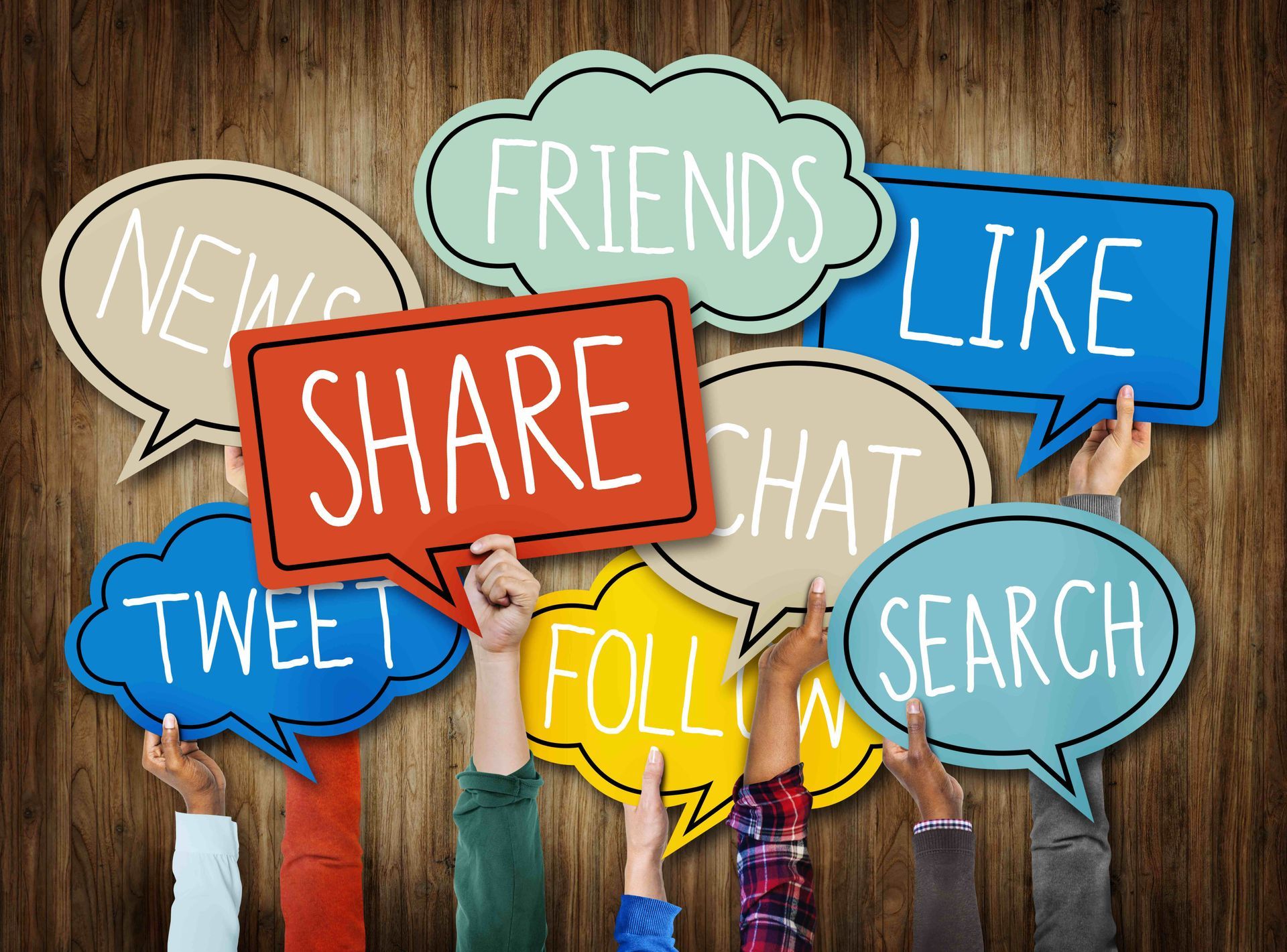 Hands holding colorful speech bubbles with social media terms against a wood background.