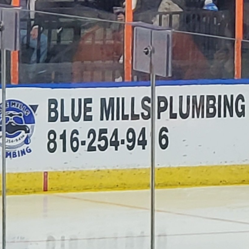 A blue mills plumbing sign on the side of a hockey rink