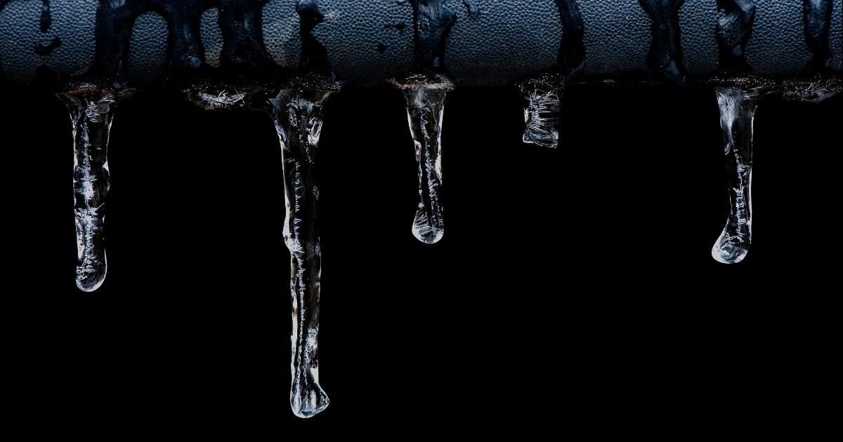 Icicles hanging from a dark surface with water droplets, against a black background.