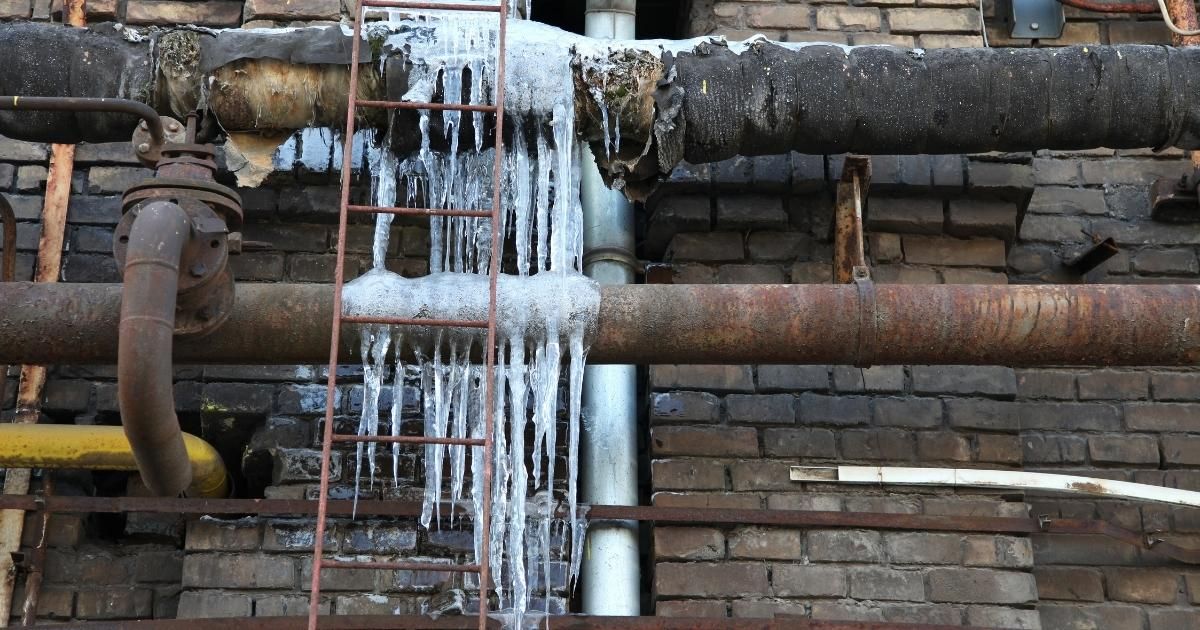 Icicles hanging from insulated pipes near a brick wall, with a small metal ladder.
