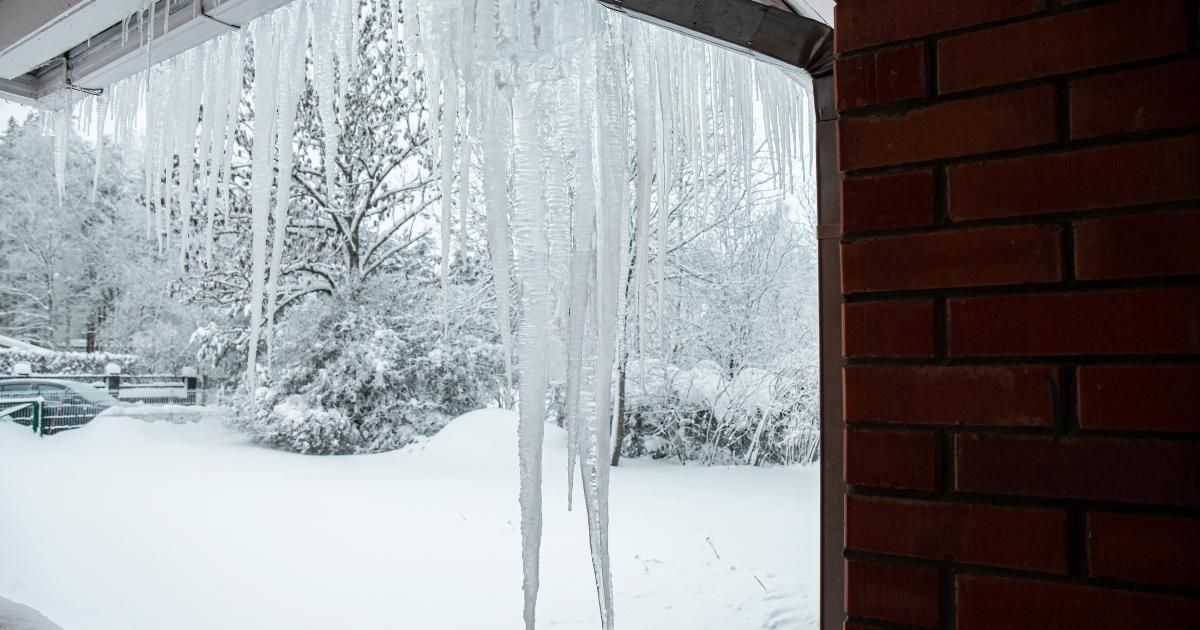 Icicles hanging from a roof edge; snowy winter landscape visible outside.