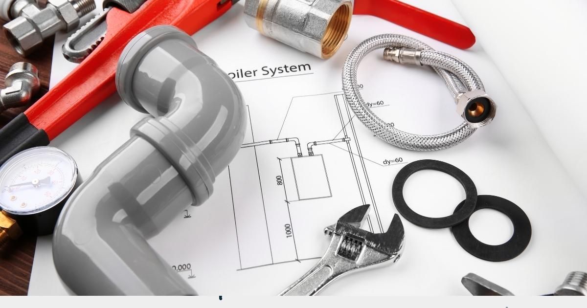 Plumbing tools and parts including pipes, wrench, and diagram on a work surface.
