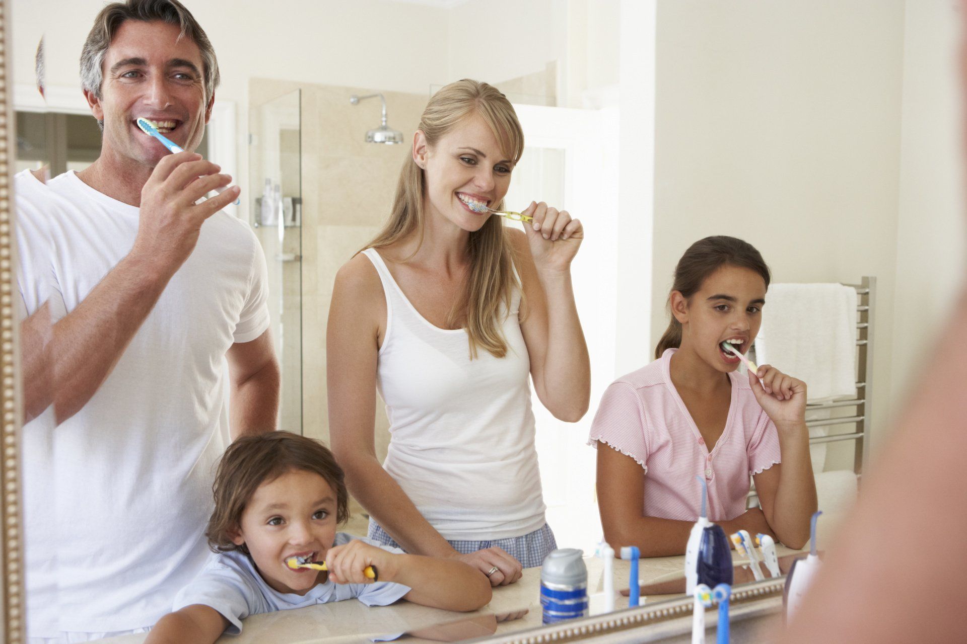 Family of four brushing their teeth in front of a mirror