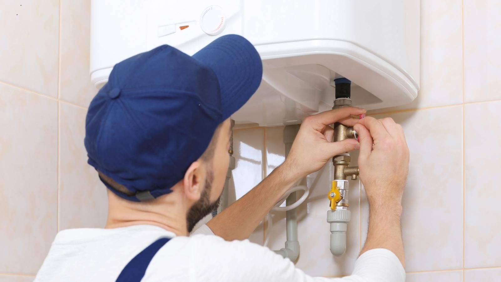 A man is fixing a water heater in a bathroom.