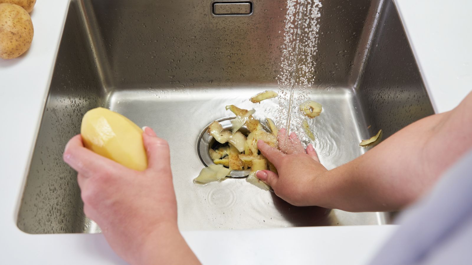 A picture showing hands placing potatos down a garbage dispoal 