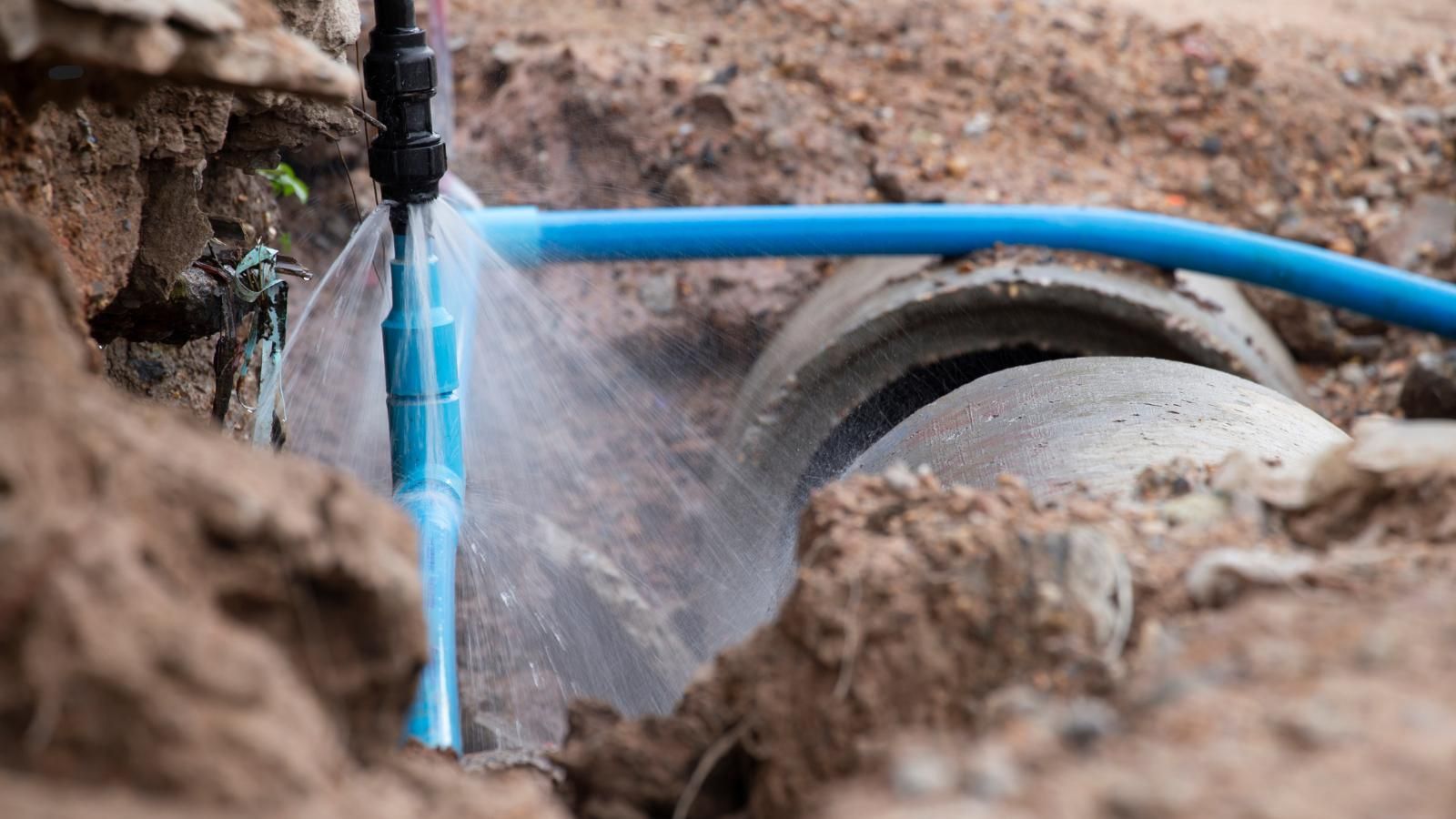 A hose is spraying water on a water main pipe in the dirt.