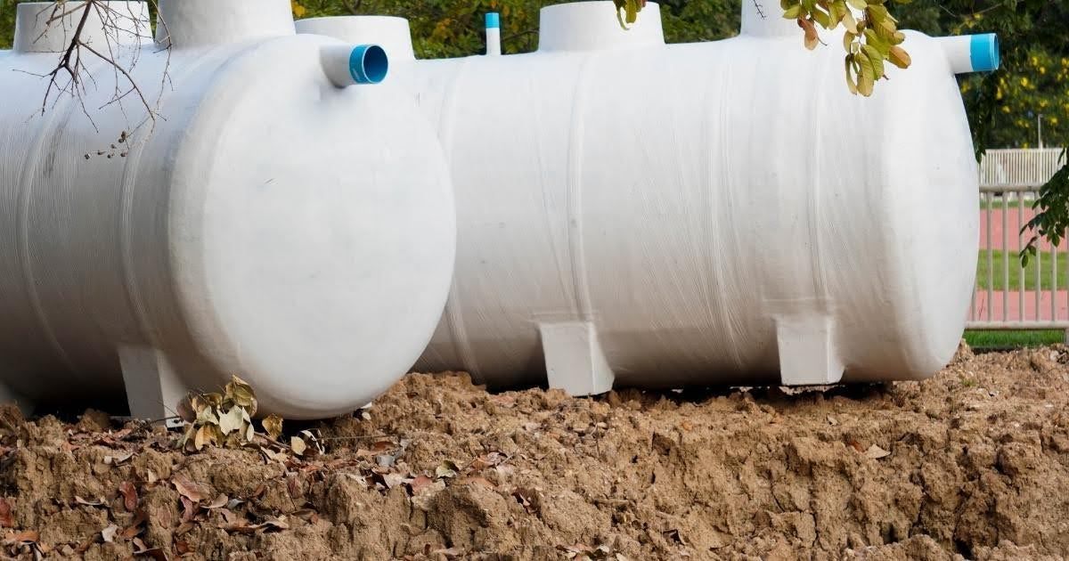 A large black septic tank is sitting in the dirt in a trench.