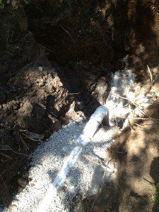 A pipe is laying in the dirt in a hole.