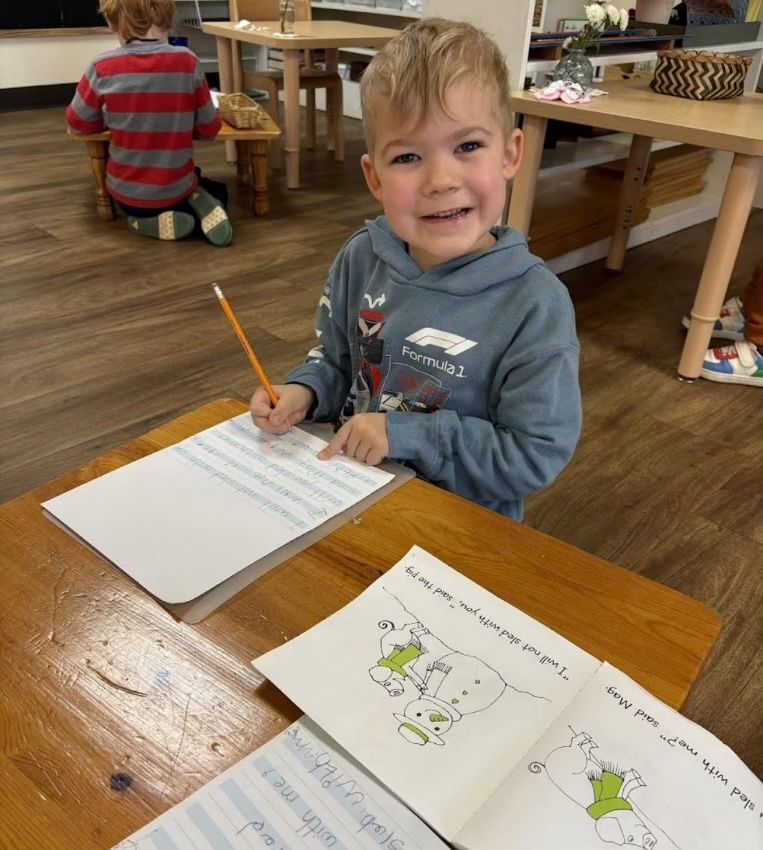 A young child is sitting at a table, holding a pencil above a piece of paper.
