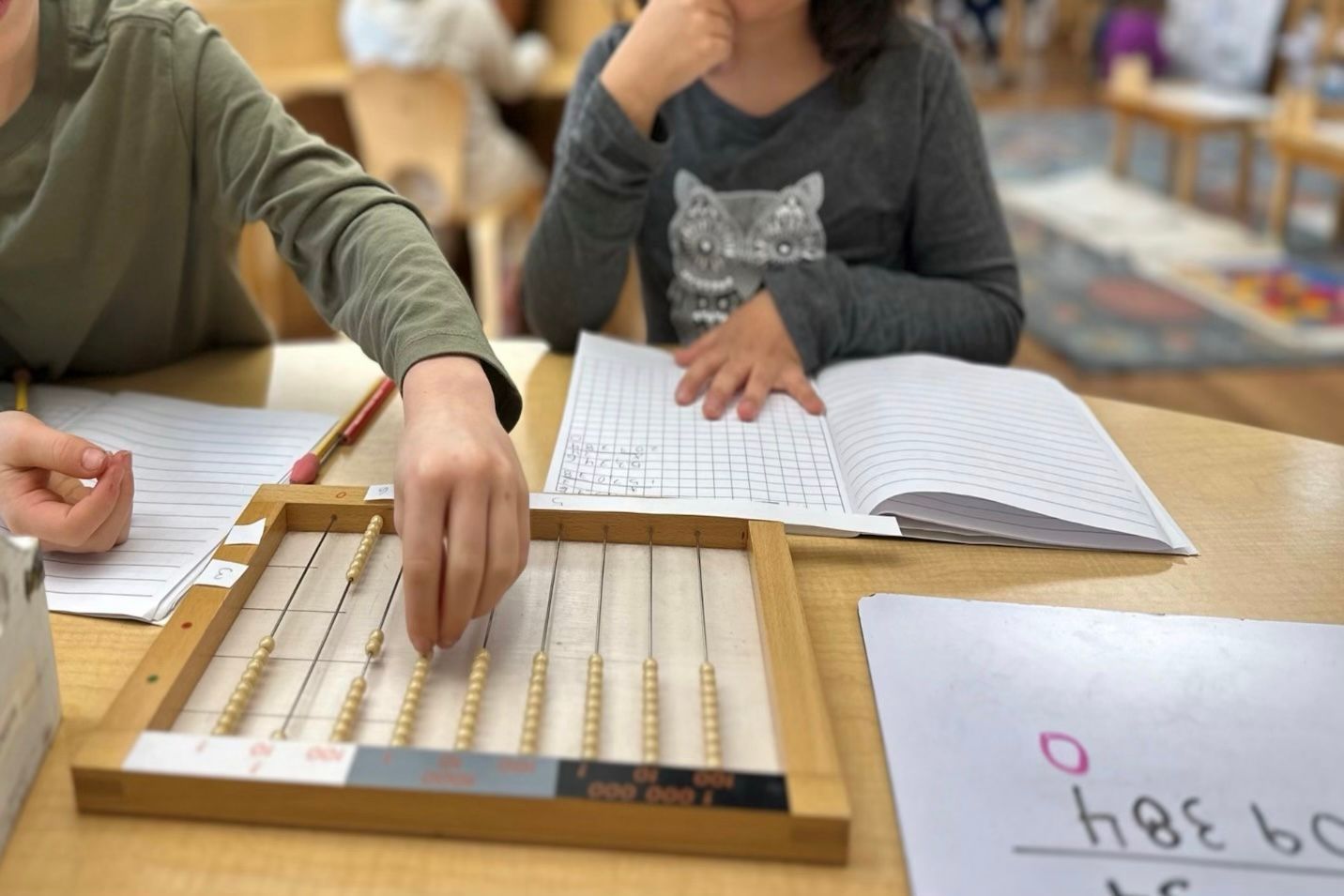 Two children working together at a table, with a flat bead frame in front of them.