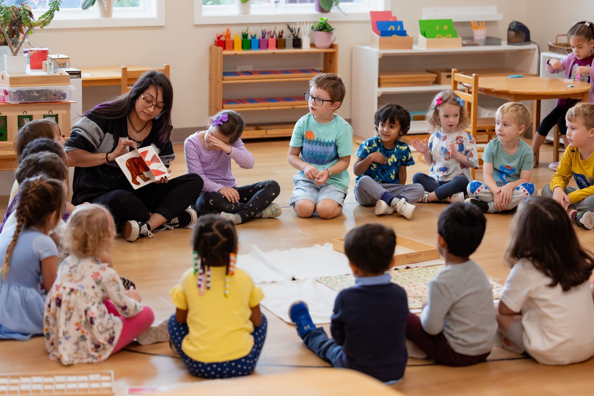 Teacher reading to a circle of children in a bright classroom, with kids sitting on the floor around her.