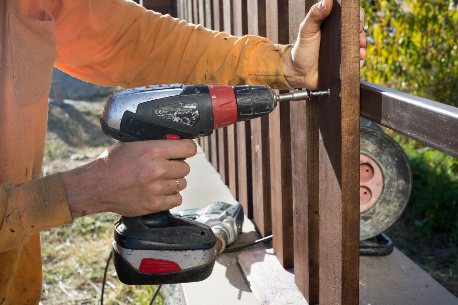 A man is using a drill to fix a wooden fence.