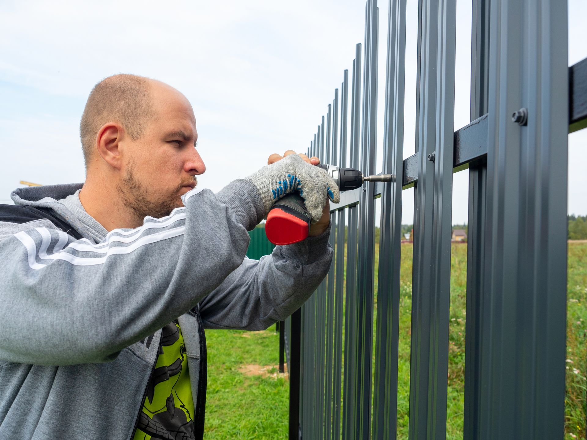 A man is installing a metal fence with a drill.