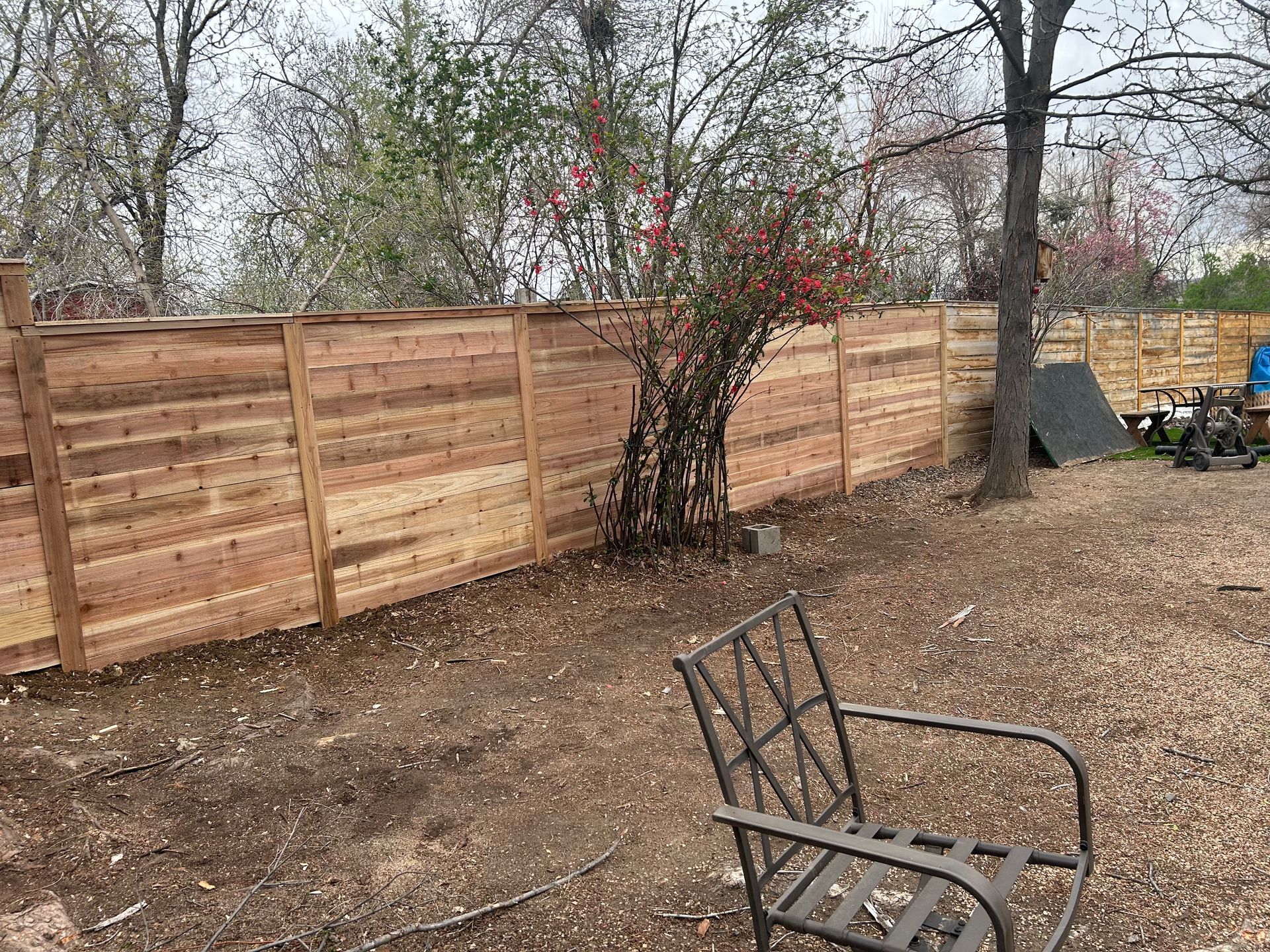 There is a wooden fence in the backyard with a chair in front of it.