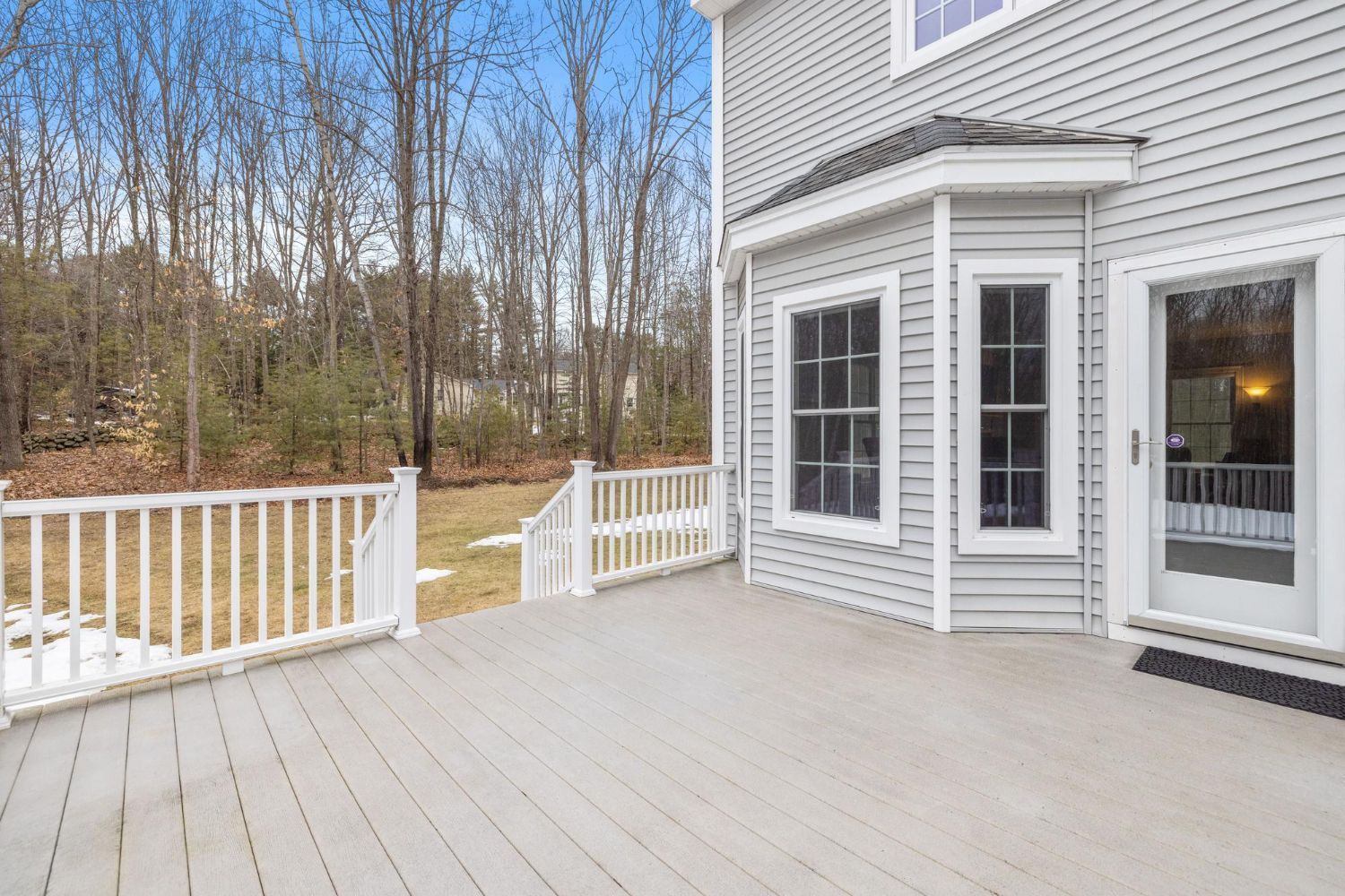 There is a large deck in front of a house with trees in the background.
