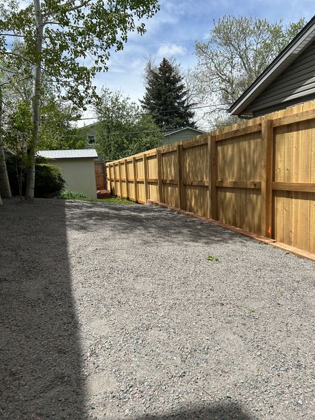 A wooden fence surrounds a gravel driveway in front of a house.